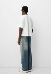 White cotton t-shirt with short sleeves, paired with oversized, faded blue denim jeans. Neutral background highlights the outfit's features.