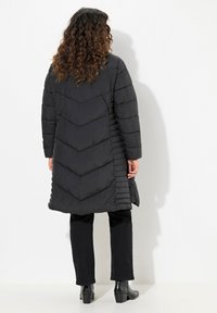 Lång svart pufferjacka med ett chevron-quiltat mönster, sidodetaljer och en avslappnad passform. Matchas med svarta byxor och ankelskor.