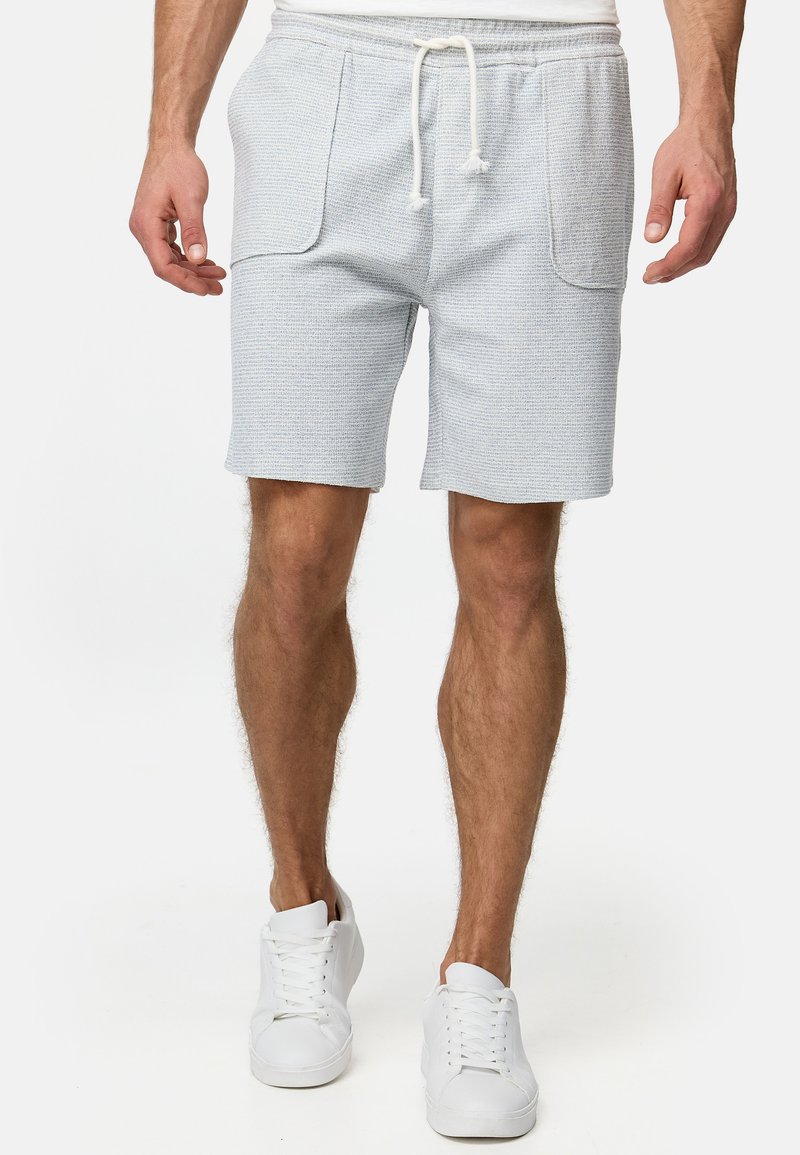 Shorts gris clair avec un motif texturé, poches latérales et une taille élastique avec un cordon de serrage. Associés à des baskets blanches.