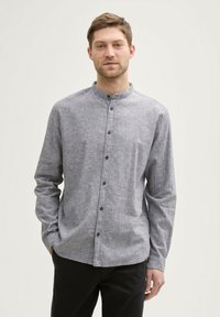 Chemise grise à manches longues avec col montant, devant boutonné et tissu texturé discret. Dotée de boutons noirs et d'une coupe ajustée.
