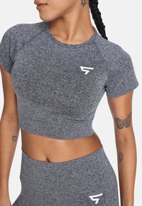 Top atlético corto gris de manga corta, con una tela texturizada y acento de logo blanco. Combinado con pantalones gris de cintura alta.