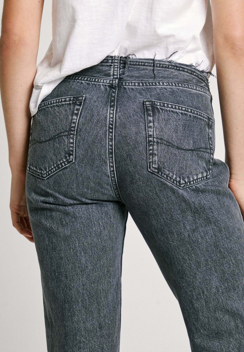 Graue Denim-Jeans mit hoher Taille, fünf Taschen und einem rohen Saum, die eine klassische Passform und eine robuste Textur zeigen.