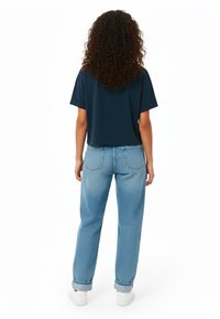 Mornarska skrajšana majica s kratkimi rokavi, združena s svetlo modrimi denim jeansami ravne kroja, ki imajo klasičen dizajn s petimi žepi in zavihanimi robovi.