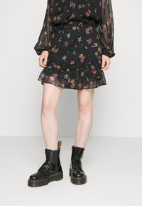 Vestido negro con flores, con mangas largas transparentes y dobladillo con volantes, que presenta patrones florales multicolores. Combinado con botas negras de suela gruesa con cordones.