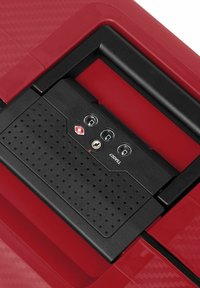 Valigia rigida rossa con superficie testurizzata. Dotata di un lucchetto approvato dalla TSA in nero e tre combinazioni su un elegante pannello incassato.