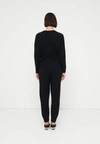 Μαύρη ολόσωμη φόρμα με ανάγλυφο πλεκτό σχέδιο, μακριά μανίκια και εφαρμοστά, στενά πόδια, με γραμμή στη μέση. Συνδυάζεται με μαύρα αθλητικά παπούτσια.