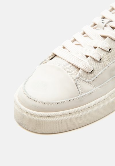 Μπέζ καθημερινό αθλητικό παπούτσι με παχιά λαστιχένια σόλα, επάνω μέρος από ύφασμα και δέρμα και λευκά λεπτά κορδόνια δεμένα σε ουδέτερο φόντο.
