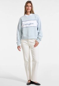 Valkoinen huppari, jossa on vaaleansininen osa ja tummansinisiä saumoja, jossa on "GUESS JEANS 1981" -logo. Yhdistetty valkoisiin suoriin farkkuihin ja mustiin ballerinoihin.