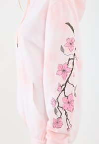 Felpa rosa con una texture morbida. Presenta fiori rosa e rami ricamati sulla manica sinistra, tasca a marsupio e cappuccio con coulisse.
