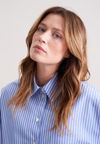 Camicia a righe blu e bianche con colletto, caratterizzata da una superficie liscia e cinque bottoni sul davanti.