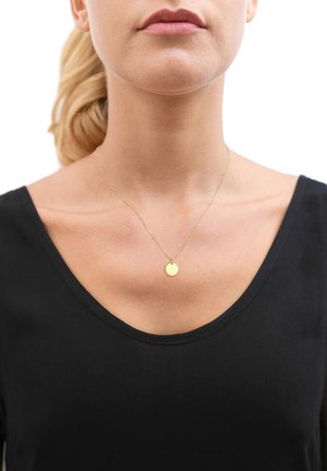 Goldene Halskette mit einem kleinen runden Anhänger, der über einem schwarzen V-Ausschnitt-Oberteil getragen wird. Einfaches Design mit einer zarten Kette und glatter Anhängersfläche.