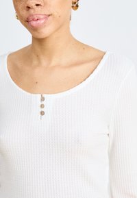 White textured long-sleeve top with a wide scoop neckline and three wooden button accents along the front.