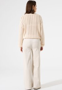 Pull en maille beige clair avec un design ajouré, manches longues, associé à un pantalon crème à jambes larges ; décontracté, tissu texturé.