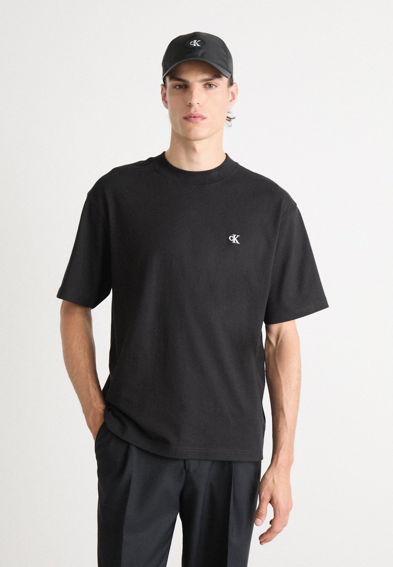 T-shirt in cotone nero con maniche corte e scollatura a girocollo. Presenta un piccolo logo CK bianco sul petto sinistro. Abbinato a pantaloni neri.
