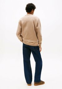 Beige sweatshirt met een gestructureerde afwerking, ronde halslijn en ribgebreide manchetten, gecombineerd met donkerblauwe losse jeans en bruine casual schoenen.