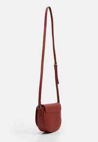 Bolso cruzado de cuero rojo con textura suave, forma redondeada, correa ajustable y cierre con solapa. Diseño simple con hardware mínimo.