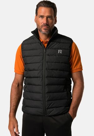 Schwarze gefütterte Weste mit hohem Kragen und Reißverschluss, mit einem Logo auf der Brust. Trägt man über einem orangefarbenen Poloshirt.