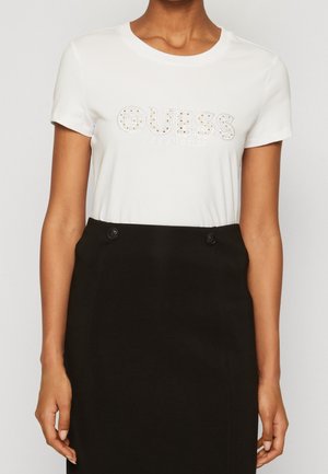 Woman wearing a white short-sleeve t-shirt with "GUESS Los Angeles" text and a high-waisted black skirt with button details.