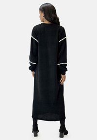 Abito maxi in corduroy nero con maniche lunghe, bordo decorativo bianco sulle maniche e una vestibilità dritta e rilassata. Presenta uno spacco laterale e una texture a coste.