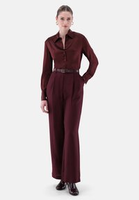 Burgundy satin blouse with button-down front, paired with high-waisted matching trousers. Accessories include a brown belt and earrings.