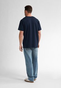 Tmavě modré bavlněné tričko s krátkými rukávy, volný střih. V kombinaci se světle modrými džíny a bílými teniskami s hnědými podrážkami.