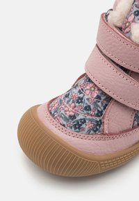 Chaussures roses avec une tige en tissu floral ornée de petites fleurs roses et bleues, maintenues par deux bandes Velcro, et dotées d'une semelle en caoutchouc.
