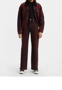 Chaqueta de mezclilla burdeos con un collar de piel sintética negra, combinada con unos pantalones vaqueros de pierna ancha a juego. Con un dobladillo con flecos notable y zapatillas negras.