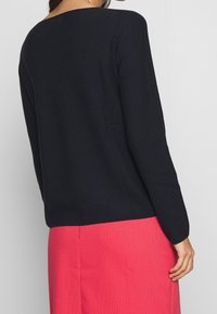 Maglione nero a coste con scollatura ampia e maniche lunghe, abbinato a una gonna rosa brillante con un motivo strutturato.