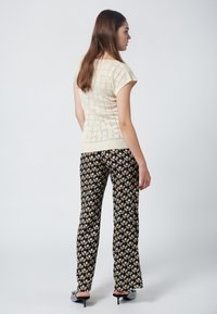 Krämfärgad stickad topp med korta ärmar, matchad med svarta mönstrade vida byxor med geometriska mönster i gult, beige och vitt.