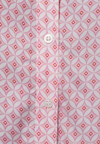 Light pink shirt fabric features a geometric pattern of overlapping circles and diamond shapes in darker pink and red hues. White buttons present.