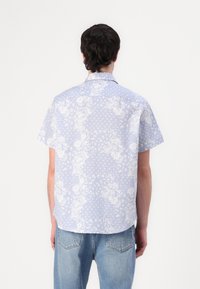 Camicia a maniche corte in tessuto azzurro chiaro con motivi floreali bianchi e pois; vestibilità comoda con colletto.