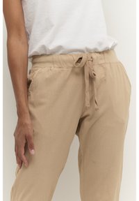 Beige joggers met een trekkoord, gemaakt van zachte, gestructureerde stof. Voorzien van een elastische tailleband en zijzakken, met een relaxte pasvorm en taps toelopende benen.