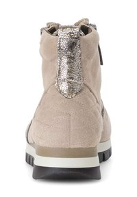 Beige suède enkellaars met een gewatteerd ontwerp, een zilver gemêleerde band aan de achterkant en een zwarte rubberen zool met lichtgrijze accenten.