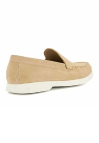 Beige suède instapper met een ronde neus, witte rubberen zool en zichtbare stiknaad langs de bovenrand. Zachte textuur.