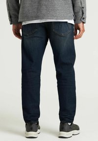 Sötétkék, slim fit farmernadrág sima textúrával, két hátsó zsebbel és közepes derékmagassággal. Szürke sportcipővel párosítva.