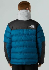 Giacca a vento blu e nera con cappuccio grigio staccabile; presenta sezioni a righe orizzontali e un logo sulla parte superiore sinistra della schiena.