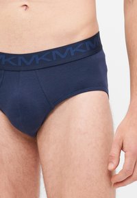 Des slips pour homme bleu marine avec une ceinture élastique texturée présentant des lettres répétées. Fabriqués en tissu lisse avec une coupe ajustée.