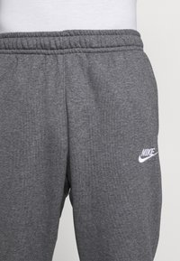 Grå Nike sweatshorts med elastisk midja, med en vit logotyp på vänster sida. Tyget har en mjuk, texturerad yta.