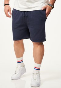 Marineblaue Baumwollshorts mit elastischem Bund und Kordelzug. Kombiniert mit weißen Turnschuhen und gestreiften Crew-Socken in Rot, Weiß und Blau.