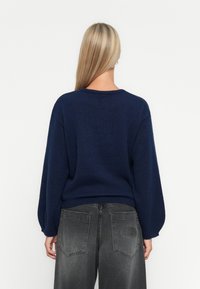 Navyblauwe, chunky gebreide trui met een ronde halslijn en brede mouwen, gecombineerd met hooggemeten grijze spijkerbroeken met achterzakdetails.