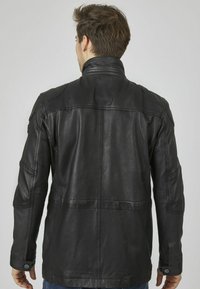 Giacca di pelle nera con colletto alto, cuciture visibili e polsini con bottone. Texture liscia e design semplice, adatta per un abbigliamento casual.