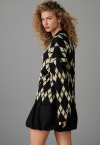 Pull en tricot noir et ivoire avec un motif de losanges, doté de manches longues et d'une coupe décontractée. Associé à une jupe noire superposée.