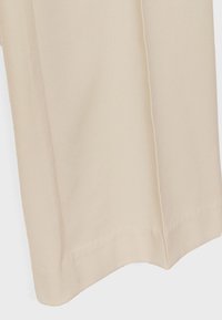 Beżowa tkanina, gładka tekstura, szeroki krój, czyste wykończenia i boczne szwy. Brak widocznych wzorów ani detali metalowych.