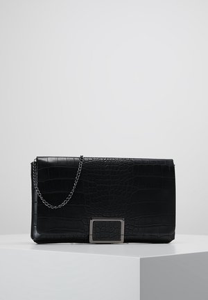 Pochette en cuir noir à texture crocodile, bandoulière chaîne argentée et détail boucle rectangulaire argentée, posée sur un socle blanc.