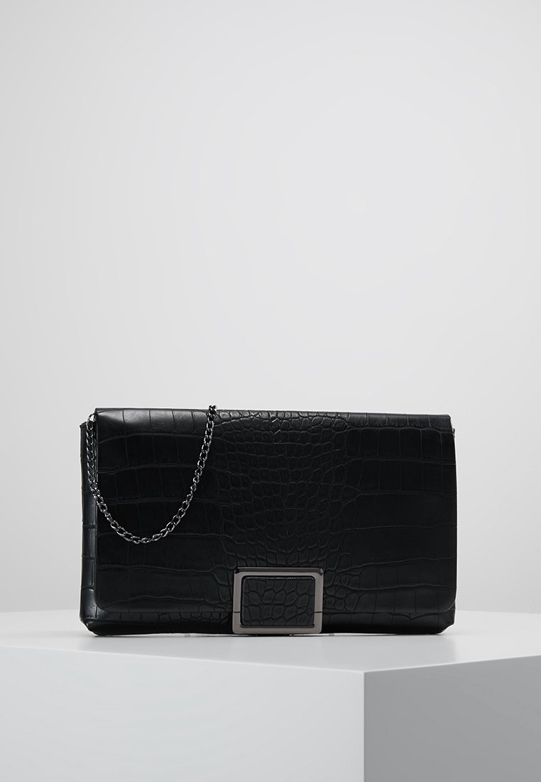Pochette en cuir noir à texture crocodile, bandoulière chaîne argentée et détail boucle rectangulaire argentée, posée sur un socle blanc.
