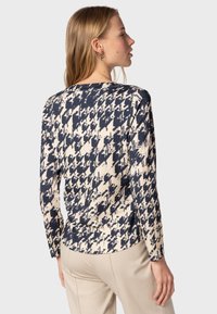 Haut à manches longues en crème et bleu marine avec un motif pied-de-poule. Présente un col rond et une silhouette ajustée. Texture de tissu lisse et douce.