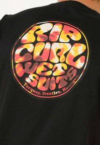 Camisa negra con un gran gráfico circular en naranja brillante y amarillo, con letras onduladas que dicen "RIP CURL WET SUIT."