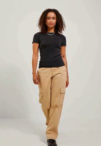 Top corto de manga corta negro de canalé combinado con pantalones cargo beige que cuentan con bolsillos laterales. La modelo se presenta con confianza sobre un fondo neutro.