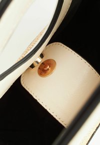 Gros plan de l'intérieur d'un sac en cuir beige avec fermeture à bouton-pression doré et doublure en tissu noir.