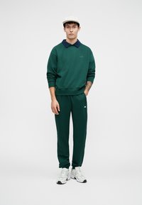 Groene sweatshirt met een marineblauwe kraag, gecombineerd met bijpassende groene sweatpants. De outfit heeft een subtiel logo en is gemaakt van zacht materiaal.